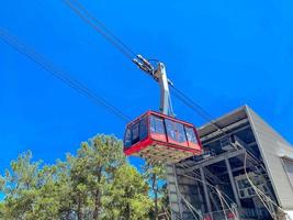 cable car on the mountain. cabin with tourists moves on black, thick cables from the depot, aerial tour of the blue sky. red cabin with large windows for visibility photo