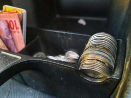 Some rupiah coins and one hundred thousand rupiah notes and some other money in a box provided on the dashboard of the car photo