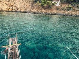 yate en mar abierto. mar con una playa de arena con el telón de fondo de una montaña, grandes piedras en el fondo. en un yate un puente de madera con pasamanos de metal foto