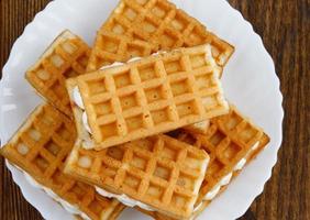 A pile of ruddy Viennese waffles lie on a white plate on a wooden background. photo