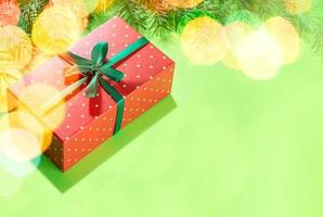 caja rectangular roja envuelta en lunares en verde con luces navideñas. regalo bajo el árbol de navidad. foto