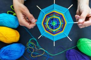 Hands of young girl keepmandala of multicolor yarn threads on grey background. photo