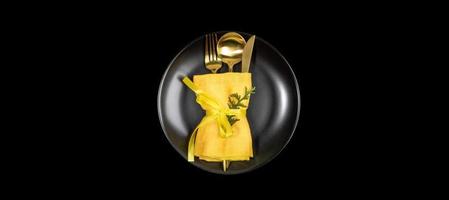 Xmas table setting banner with golden cutlery set on round black plate in center of black. photo