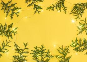 Frame of green arborvitae branches and luminous Xmas lights on yellow background with copy space in center. Xmas decor. photo