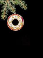 una decoración de navidad donut de vidrio colorido colgando de ramas de abeto verde sobre fondo vertical negro. foto