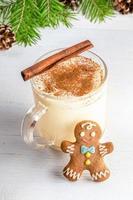 Homemade Xmas eggnog with cinnamon in glass cup with ginger man on white wooden backdrop. photo