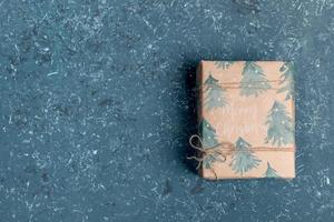 One gift box wrapped in festive Xmas wrapping paper on turquoise textured background. Top view. Copy space. photo
