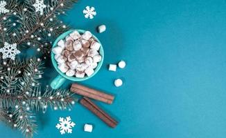 Turquoise Christmas background with fir branches with snow and cup of coffee or cocoa with marshmallows. Top view. photo