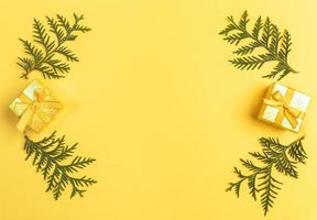 Xmas greeting card with frame of gift boxes and green arborvitae branches laid out on yellow with copy space in center. photo