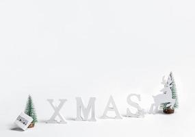 Xmas festive trendy minimal background. Christmas decorations letters XMAS, Xmas trees, deer, DIY gift box on white. photo