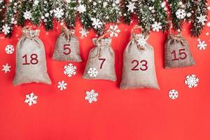 Xmas advent calendar - canvas sacks with numbers on fir tree branches, snowflakes and snow on red. photo