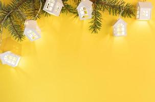 Xmas yellow background with frame of green fir branches and luminous Xmas lights on bright yellow with copy space. photo