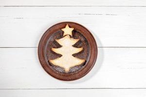 Homemade cookie as Christmas tree on round brown plate on white wooden backdrop with copy space. photo