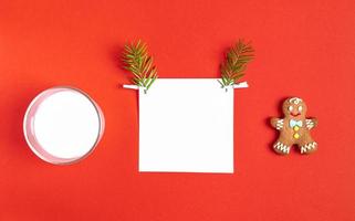 White square sheet with fir twigs as reindeer face, milk glass and gingerbread man on red backdrop. photo