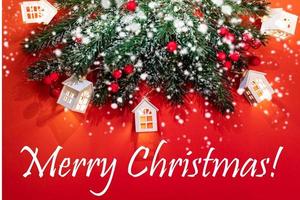 tarjeta de felicitación de navidad con ramas de abeto, luces de navidad cabañas blancas, nieve, bokeh en rojo con la leyenda feliz navidad. foto