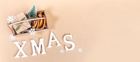 vista superior caja de madera con adornos navideños y letras blancas xmas en beige. pancarta de navidad foto