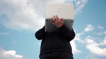guy travaille sur un ordinateur portable dans un parc de la ville sur fond de ciel magnifique. un pigiste masculin utilise un ordinateur portable pour le travail en extérieur. notion de travail à distance. la caméra tourne à 360 degrés. ralenti. video