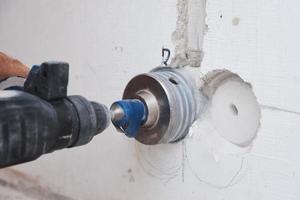 Builder with hummer drill perforator drills hole in a wall photo