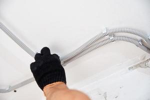 Electrician fixing electric cable to the wall, closeup photo