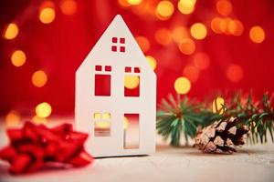 Toy house and fir tree branch against blurred bokeh lights on a red background photo