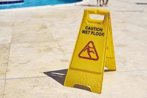 Yellow wet floor caution sign in summer day, closeup photo