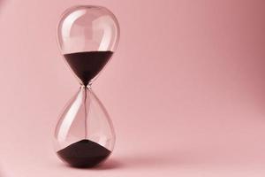 Hourglass on pink background, closeup. Urgency and running out of time concept photo