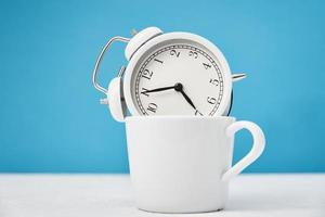 White retro alarm clock in cup on blue background. Morning time concept photo