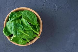 Fresh spinach leaves in wooden bowl on dark background. Organic food photo