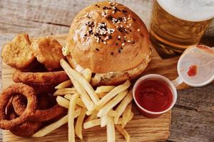 Different types of fastfood and snacks and glass of beer on the table photo