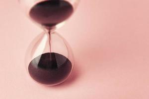 Hourglass on pink background, closeup. Urgency and running out of time concept photo