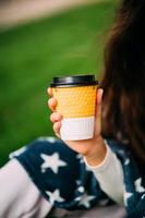 Woman's hand holding a paper glass of coffee in the park photo