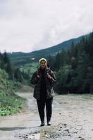 modelo de hipster femenino saludable activo senderismo a lo largo de la carretera de montaña del bosque. foto