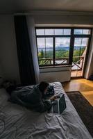 Young woman working on laptop while lying on bed photo