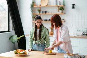 Two girlfriends cut fruit in the kitchen photo