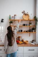 Woman takes out a glass from shelf in the kitchen photo