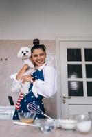 mujer sonriente en la cocina sosteniendo un lindo perro maltés blanco foto