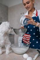 Woman in the kitchen sifts flour together with a dog photo