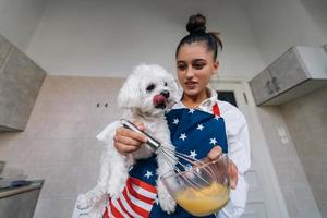 Woman is holding maltese dog while whisking an egg photo