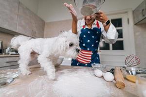 Woman in the kitchen sifts flour together with a dog photo