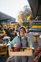 Farmer woman holds a wooden box with pumpkins in hands photo