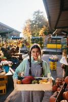 Farmer woman holds a wooden box with pumpkins in hands photo