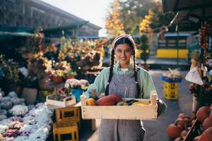 Farmer woman holds a wooden box with pumpkins in hands photo