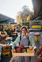 Farmer woman holds a wooden box with pumpkins in hands photo