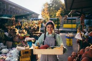 Farmer woman holds a wooden box with pumpkins in hands photo