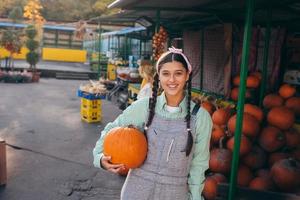 Happy farmer woman in a denim jumpsuit holds ripe pumpkin photo