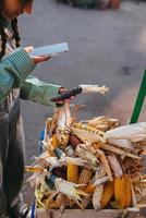 Young woman takes a photo of a corn cob at the market