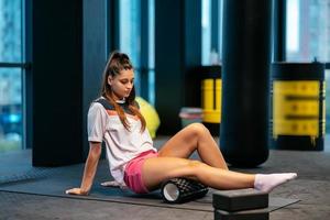 Young woman using a foam roller while doing stretching exercises photo