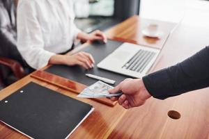 Close up view of man's hands with money indoors against woman that works by laptop photo