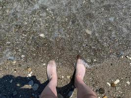 los pies de un hombre parados en la arena blanca de la playa foto