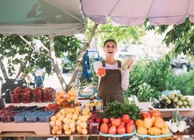 Young saleswoman holding zucchini and tomato in hands photo